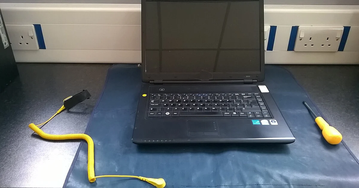 Work area prepared for maintenance on a laptop. ESD mat & wriststrap, screwdriver and laptop shown.